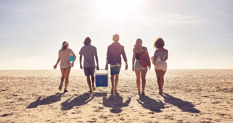 Pessoas caminhando juntas na praia, representando convivência, bem-estar e saúde integral